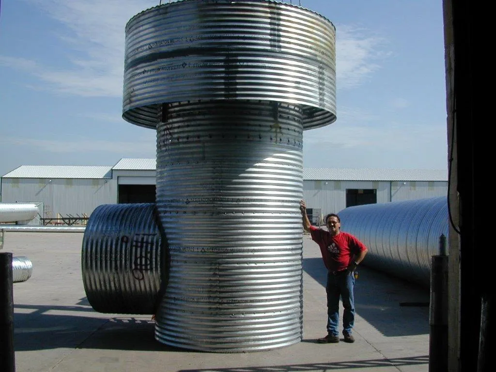 Large diameter corrugated metal bonnet riser standing in a yard, a person alongside it for scale