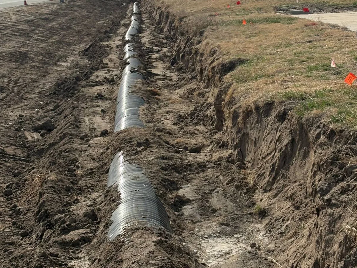 Polymer-coated galvanized corrugated metal pipe bedded in an open trench alongside a road